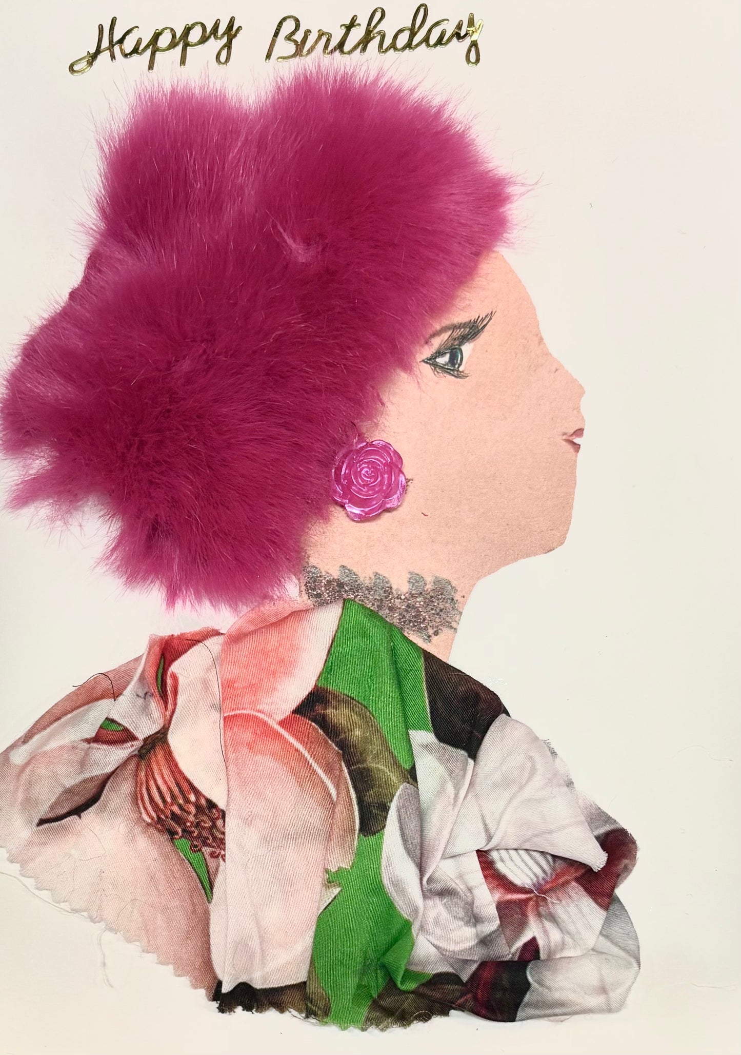 A woman wears a fuzzy hot pink hat and a multicoloured blouse with light pink and green. She wears a pink rose earring and silver necklace. Happy Birthday is written in gold at the top right corner of the card. 