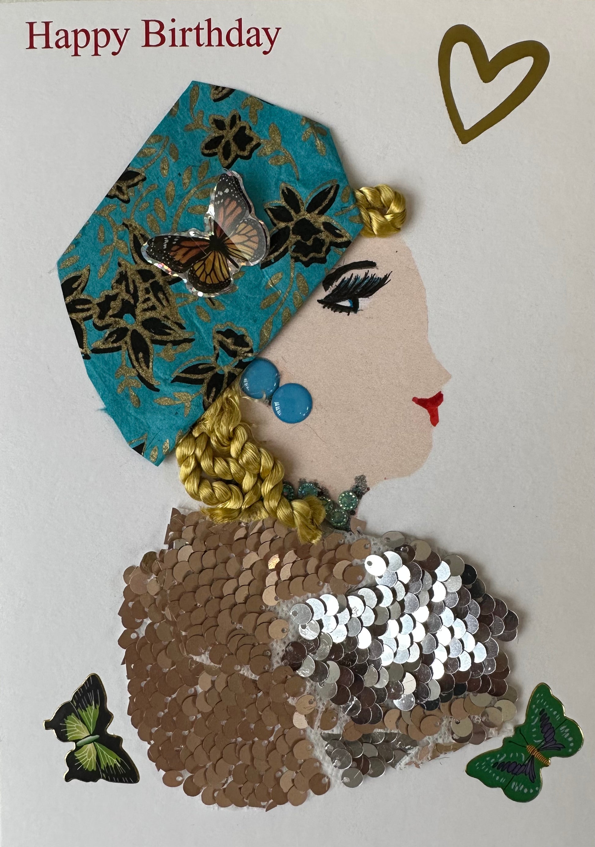 I designed this card for Gloucester Grace. This handmade card is of a woman in a bronze coloured sequin top. Her blonde hair is covered by a teal coloured cloth with black and gold flowers. There is a heart in the upper right corner as well as "Happy Birthday" and butterflies.