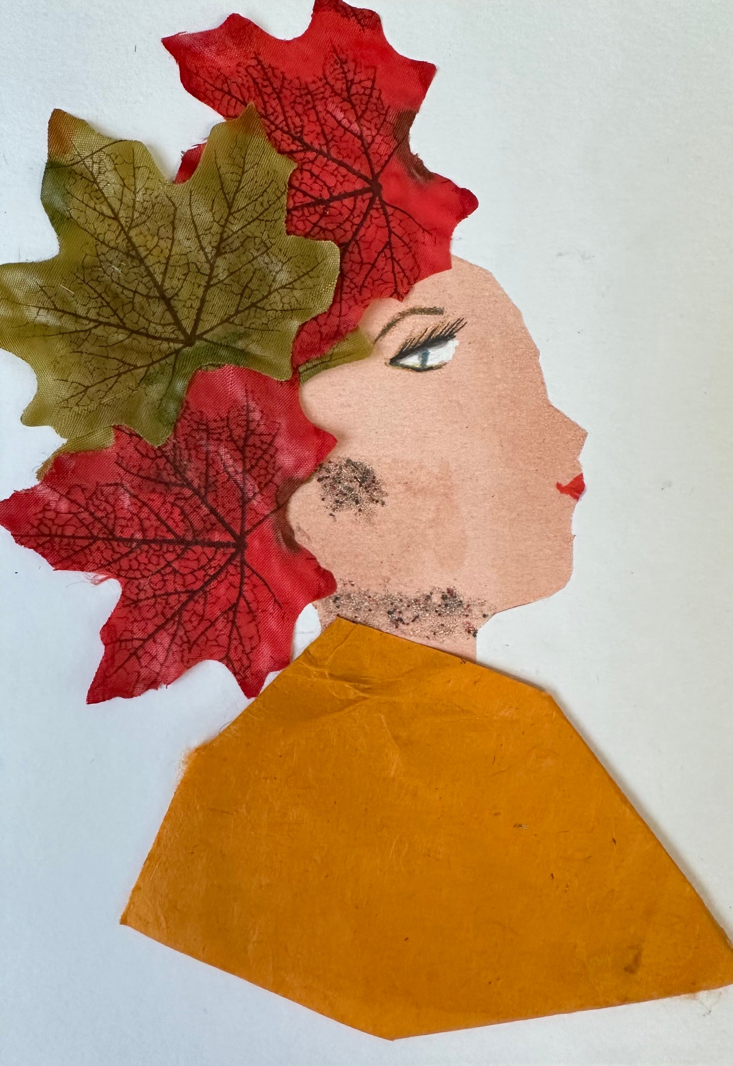 I designed this handmade card of a woman dressed in an orange blouse. Her hair is made up of three leaves, two that are red and one is green. She has jewellery that is composed of small dots.