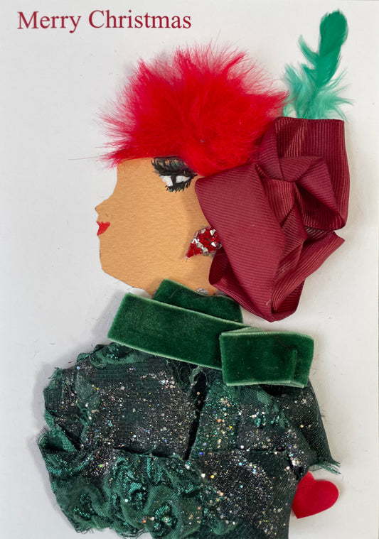 I designed this card of a woman named Blair Bermondsey. She has a white skin tone and has a shiny, dark green blouse on matched with a dark green scarf. She has a pair of festive red and silver diamanté earrings. Her bright red hair contrasts with her dark red headpiece as there is a green feather on top. It says Merry Christmas in the top left corner too. There is a red heart to the right of her. 