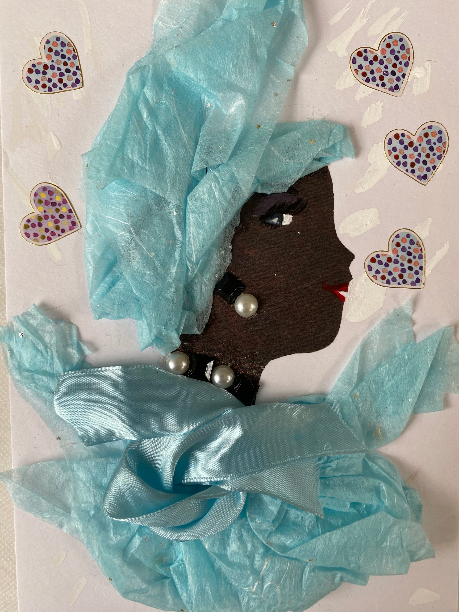 I designed this card of a woman named Brynn Blue. She has a black skin tone and wears a light blue fascinator hatinator and silk blouse with pearl jewellery. The background of the card is filled with a beautiful array of polka dotted hearts